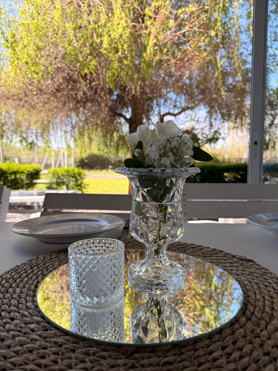 Centro de mesa con flores blancas, cristal y espejo frente al jardín